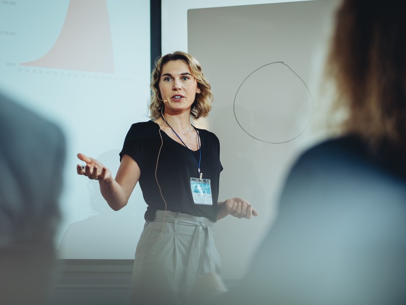 Femme d'affaires prenant la parole lors d'une conférence devant un public germanophone.